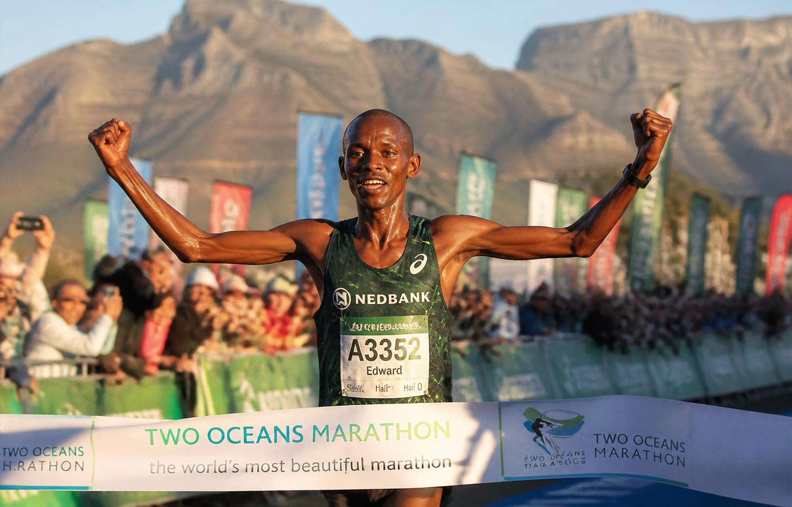 Thabo crossing the Two Oceans Marathon finish line, arms raised in triumph